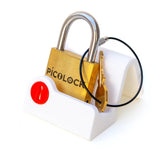 The miniature PicoLock sequential puzzle presented on a sleek white display stand. A heavy, genuine brass heirloom item that serves as an unexpected gift for gadget lovers who enjoy physical challenges.